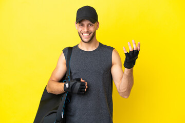 Wall Mural - Young sport blonde man with sport bag isolated on yellow background making guitar gesture