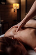 Male masseur doing back massage to client woman in dark room of massage spa