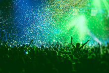 A Crowded Concert Hall With Scene Stage Green Lights, Rock Show Performance, With People Silhouette, Colourful Confetti Explosion Fired On Dance Floor Air During A Concert Festival