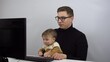 © Vital9c - The IT specialist works remotely with his son in his arms. A young man in glasses with a one-year-old son is typing on a pc.