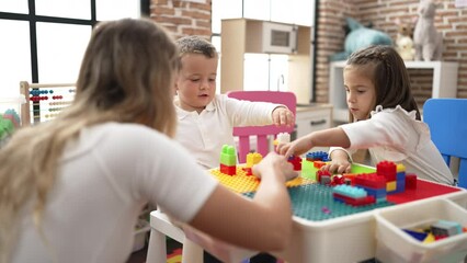 Poster - Teacher with boy and girl playing with construction blocks sitting on table at kindergarten