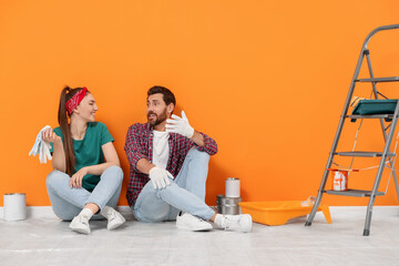 Poster - Happy designers sitting on floor with painting equipment near freshly painted orange wall indoors