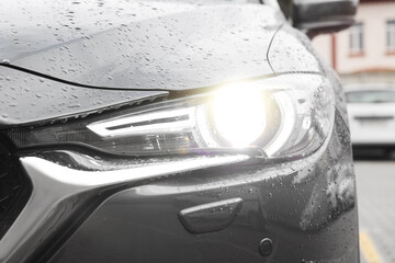 Wall Mural - Car with switched on tail light in drops of water outdoors, closeup