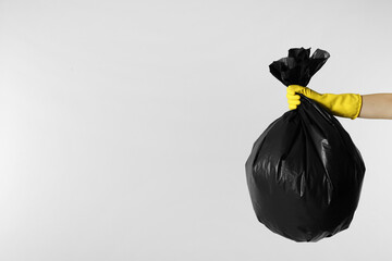 Wall Mural - Janitor in rubber glove holding trash bag full of garbage on light grey background, closeup. Space for text