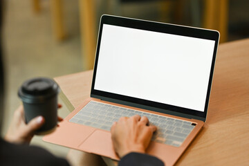 Poster - Mockup image of a Businesswoman using and typing on laptop with blank white desktop screen while holding a paper coffee cup with lid.