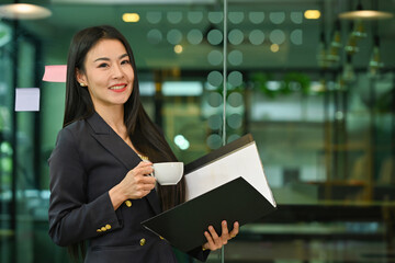 Happy Mature businesswoman holding a cup of coffee with a folder at office room.