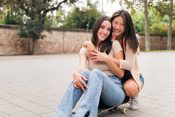 Wall Mural - portrait of a young couple of women sitting on a skateboard looking at camera, concept of love and teenager lifestyle, copy space for text