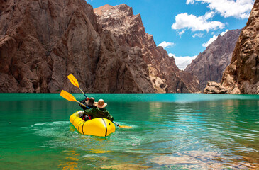 Wall Mural - Kayaking on a mountain lake. Two men are sailing on a red canoe along the lake along the rocks. The theme of water sports and summer holidays.