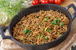 Cooked fried edible mealworms with spice and herbs in frying pan on wooden board. Meal worms as alternative protein source.