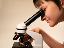 The Child Looks Into The Eyepiece Of A Microscope On A White Background. Close-up.