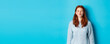 Cute redhead teen girl waiting for kiss, pucker lips and close eyes, standing in sweater against blue background