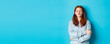 Cute redhead teen girl waiting for kiss, pucker lips and close eyes, standing in sweater against blue background