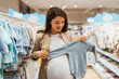 © Dusko - Beautiful young pregnant mother choosing and buying colorful clothes and appliances for her new incoming baby in. Child shop or store concept.
