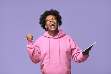 Wall Mural - Happy euphoric excited African teen winner student boy holding digital tablet computer screaming winning prize in online game, celebrating great result with yes gesture isolated on purple background.