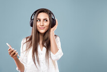 Beautiful Woman Listening To Music Using Wireless Headphones In Studio Isolated Over Blue Background.Girl Uses Wireless Earphones And Dancing