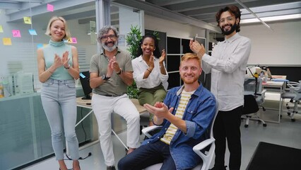 Wall Mural - Meeting of a multiracial work team applauding congratulating at a new professional success, young and mature colleagues looking at the camera with smiling expression. Group of office workers at a