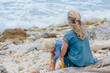 © Cavan Images - Rear view of mother with son sitting on log at beach