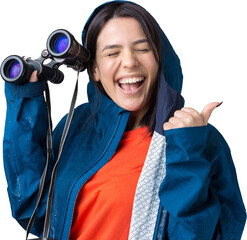 A tourist girl in a blue raincoat holds binoculars in her hands and looks into the distance, spies.