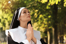 Young Nun With Hands Clasped Together Praying In Park, Space For Text