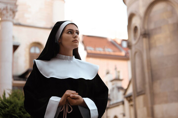 Beautiful young nun in cassock near building outdoors