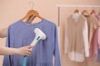 Woman steaming blouse on hanger at home, closeup. Space for text