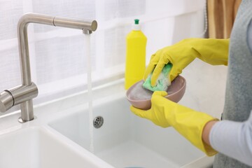 Woman washing plate above sink in modern kitchen, closeup