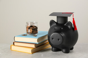 Wall Mural - Scholarship concept. Piggy bank, graduation cap, books and coins on light grey table