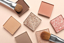 Different Beautiful Eye Shadows And Makeup Brushes On Beige Background, Flat Lay