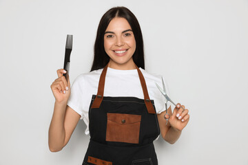 Wall Mural - Portrait of happy hairdresser with professional scissors and comb on light background