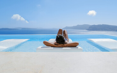 Wall Mural - Young Asian women on vacation at Santorini relaxing in swimming pool looking out over Caldera ocean