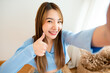 © Monster Ztudio - Pretty young asian female with big smile sitting at living room. She having fun taking light cheerful selfie on blurred background