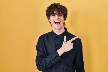 Poster - Young man wearing glasses over yellow background cheerful with a smile of face pointing with hand and finger up to the side with happy and natural expression on face