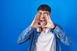 © Krakenimages.com - Young hispanic man standing over blue background shouting angry out loud with hands over mouth