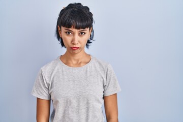 Wall Mural - Young hispanic woman wearing casual t shirt over blue background depressed and worry for distress, crying angry and afraid. sad expression.