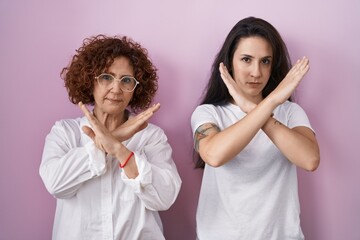 Poster - Hispanic mother and daughter wearing casual white t shirt over pink background rejection expression crossing arms doing negative sign, angry face