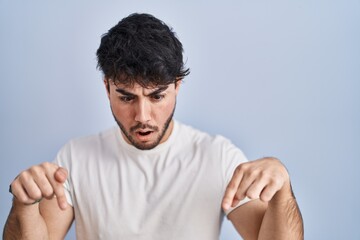 Poster - Hispanic man with beard standing over white background pointing down with fingers showing advertisement, surprised face and open mouth