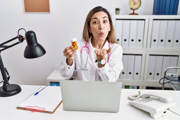 Canvas Print - Young hispanic woman wearing doctor uniform holding pills at the clinic looking at the camera blowing a kiss with hand on air being lovely and sexy. love expression.