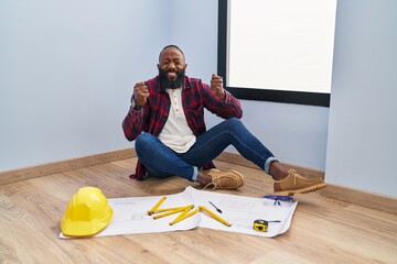 Sticker - African american man sitting on the floor at new home looking at blueprints excited for success with arms raised and eyes closed celebrating victory smiling. winner concept.