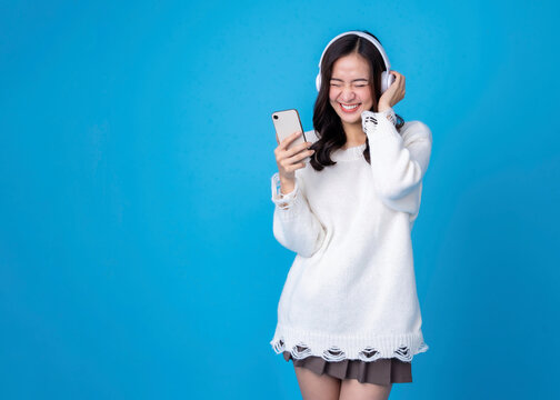 Fototapete - Happy young woman in headphones listening to music on light blue background. Smiling caucasian young woman listening to the podcast e-book music song singer rock band in headphones earphones.	