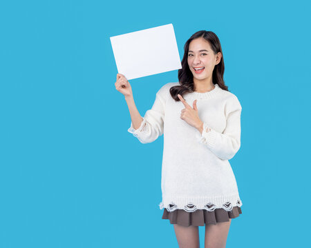 Fototapete - Your text here. Young excited woman holding empty blank board. Colorful studio portrait with light blue background. Woman holding blank empty banner pointing finger to one self smiling happy and proud