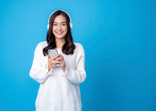 Fototapete - Happy young woman in headphones listening to music on light blue background. Smiling caucasian young woman listening to the podcast e-book music song singer rock band in headphones earphones.	