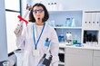 © Krakenimages.com - Young hispanic woman working at scientist laboratory holding degree scared and amazed with open mouth for surprise, disbelief face