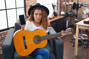 Poster - Young caucasian woman playing classic guitar at music studio holding smartphone skeptic and nervous, frowning upset because of problem. negative person.