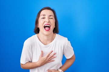 Sticker - Middle age hispanic woman standing over blue background smiling and laughing hard out loud because funny crazy joke with hands on body.