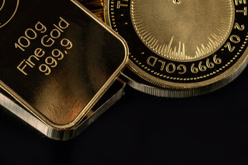 100 gram gold bar and a 2 troy ounce gold coin on a black  background.