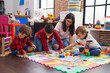 © Krakenimages.com - Teacher with group of boys playing with maths puzzle game sitting on floor at kindergarten