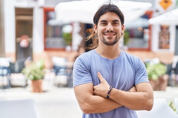 Young hispanic man smiling confident standing with arms crossed gesture at street