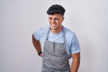 Sticker - Hispanic young man wearing apron over white background suffering of backache, touching back with hand, muscular pain