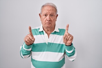 Poster - Senior man with grey hair standing over white background pointing up looking sad and upset, indicating direction with fingers, unhappy and depressed.