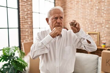 Canvas Print - Senior man with grey hair holding virtual currency bitcoin serious face thinking about question with hand on chin, thoughtful about confusing idea